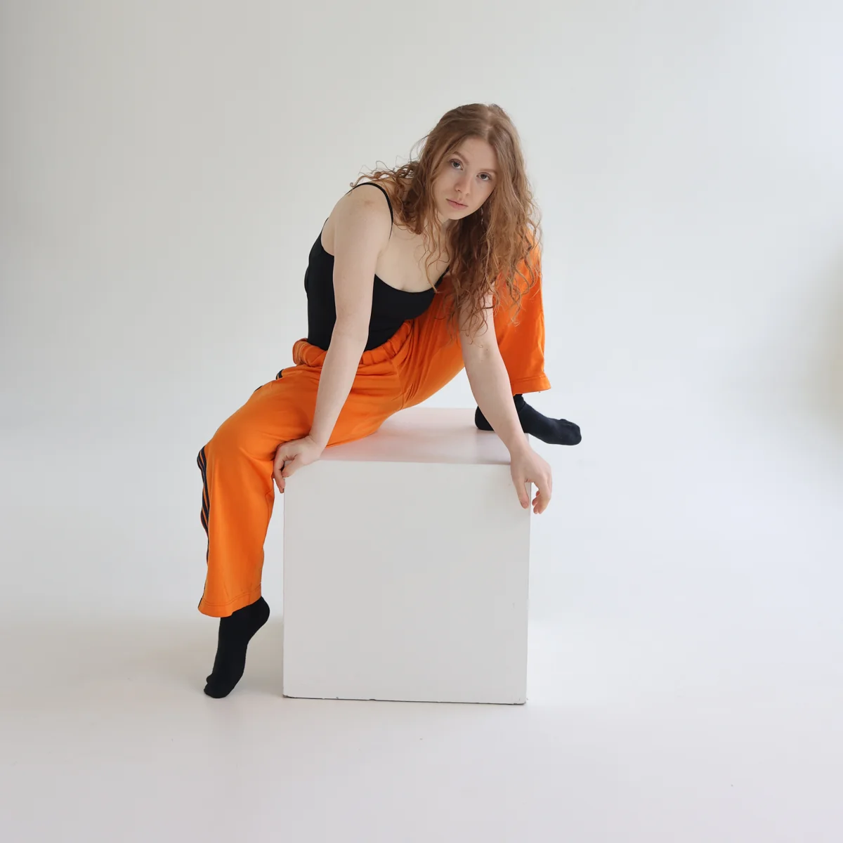 Tara in orange trousers seated on a white studio plinth