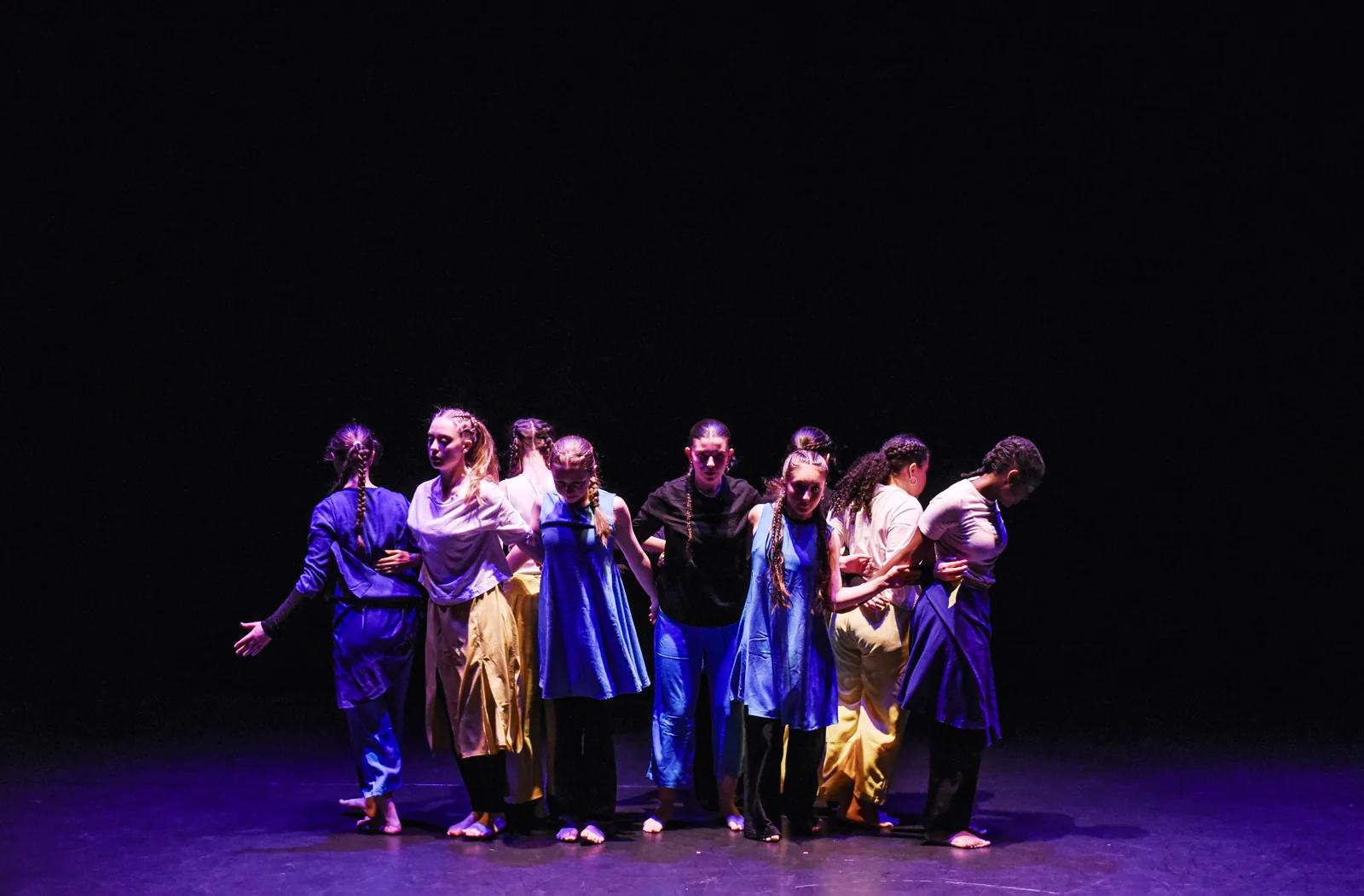 An ensemble gathered closely together under purple stage lighting