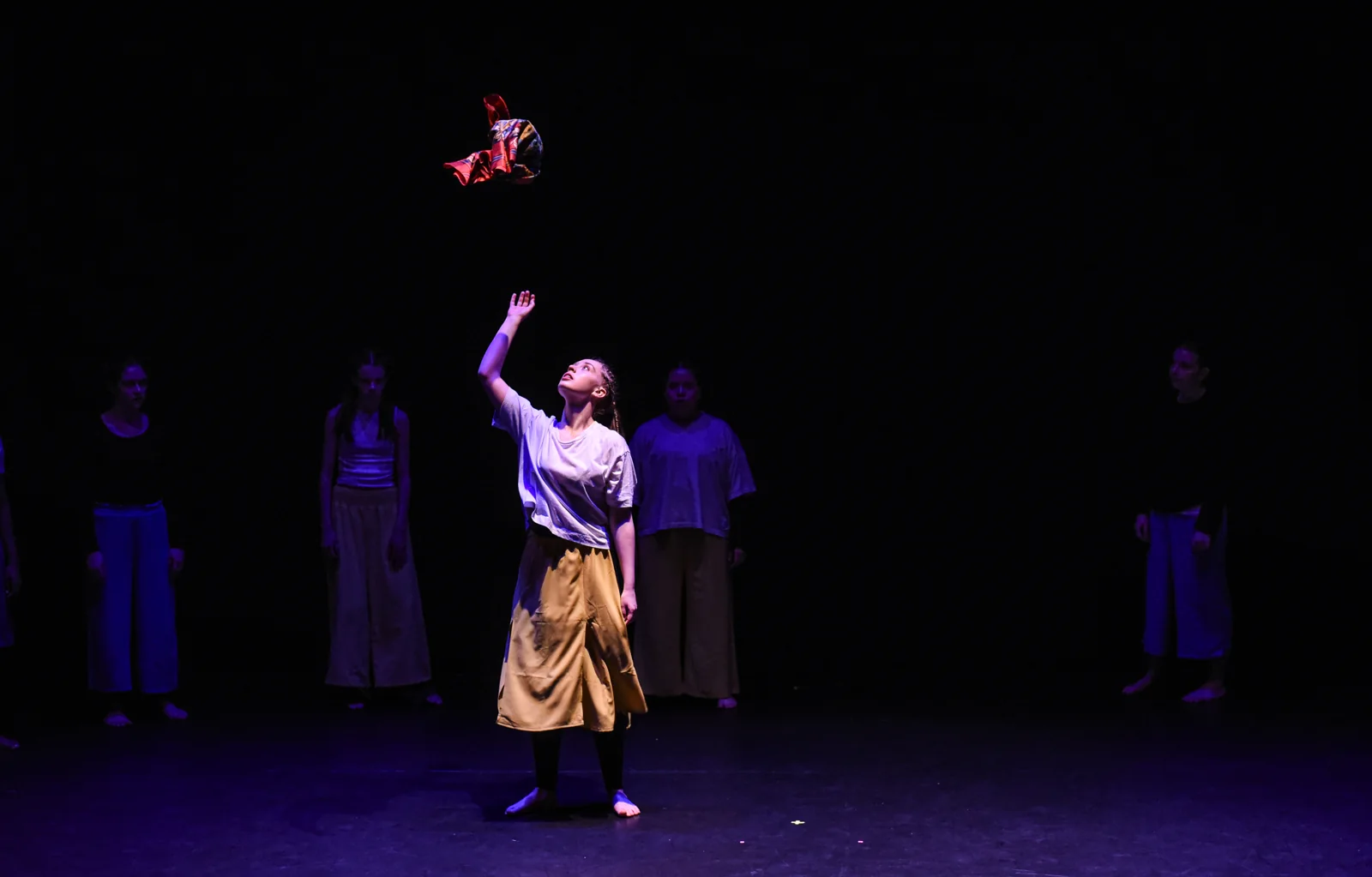 A solo dancer reaching into the light with the ensemble behind