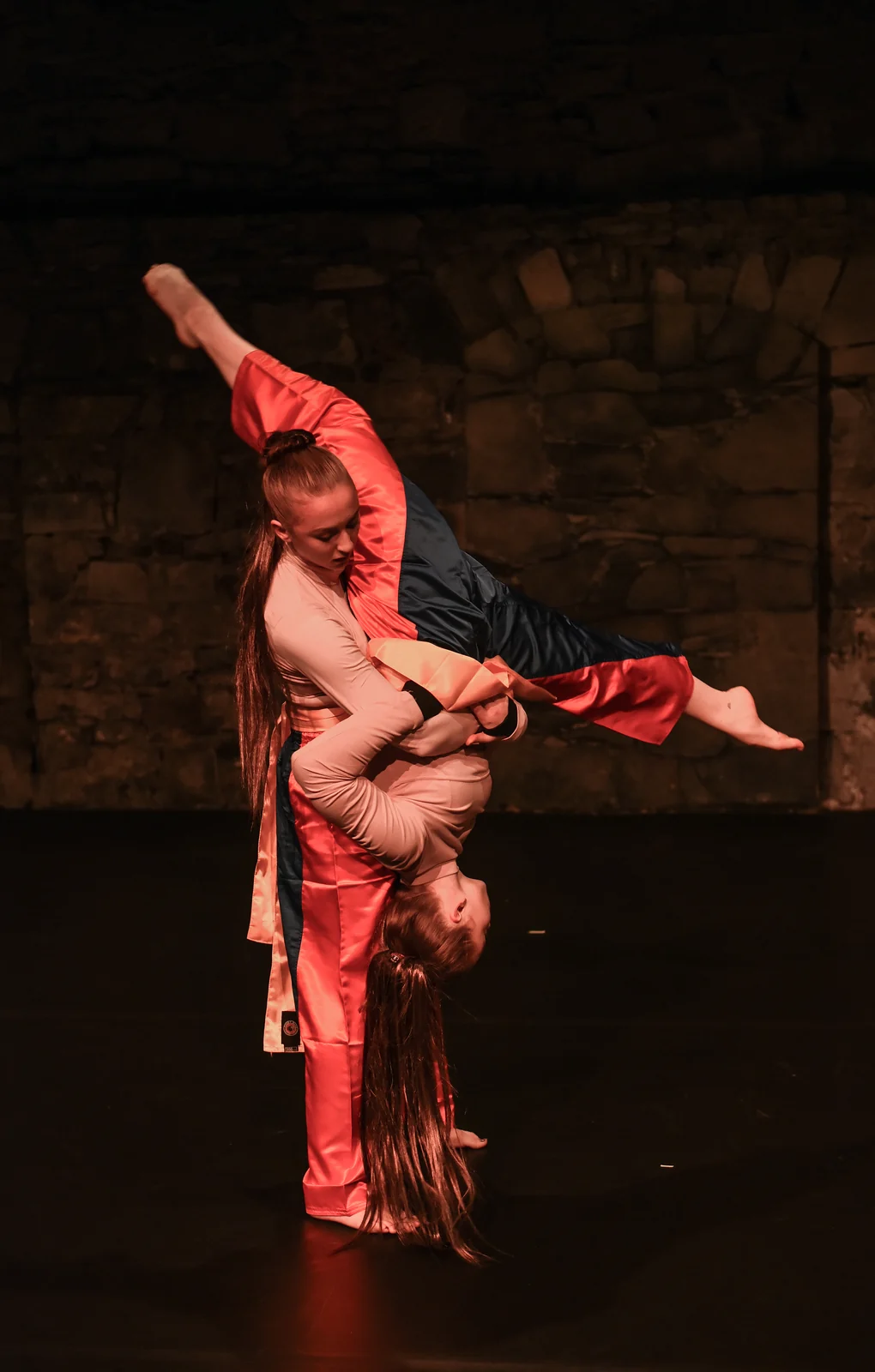 A performer dressed in red balancing in an inverted pose on stage